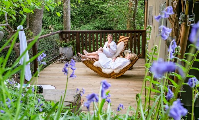 Friends relax on the deck of a safari tent in the woods.  Glamping Holidays in Wales.  Bluebells